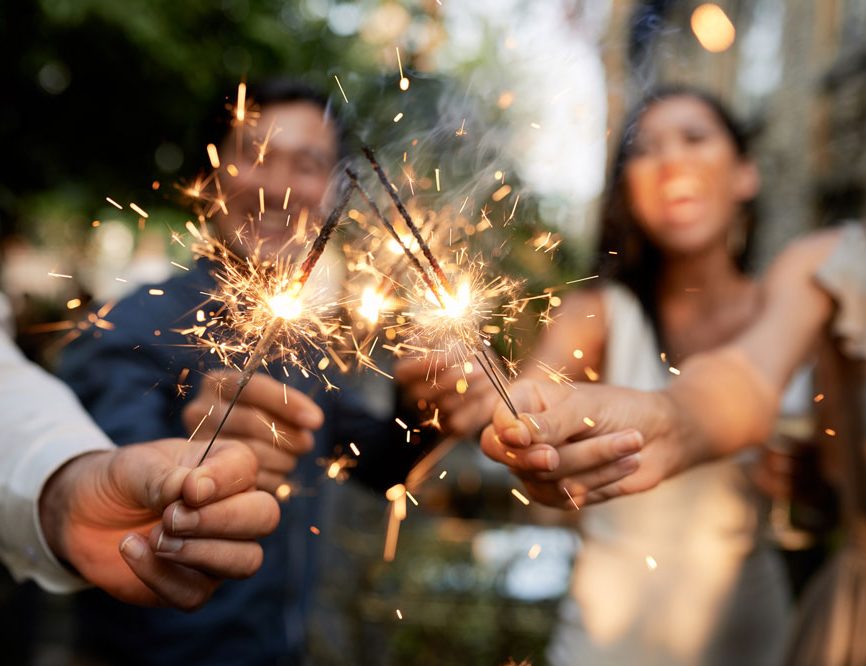 Gruppe von lachenden jungen Leuten auf einer Party, Fokus auf brennende Wunderkerzen in der Mitte